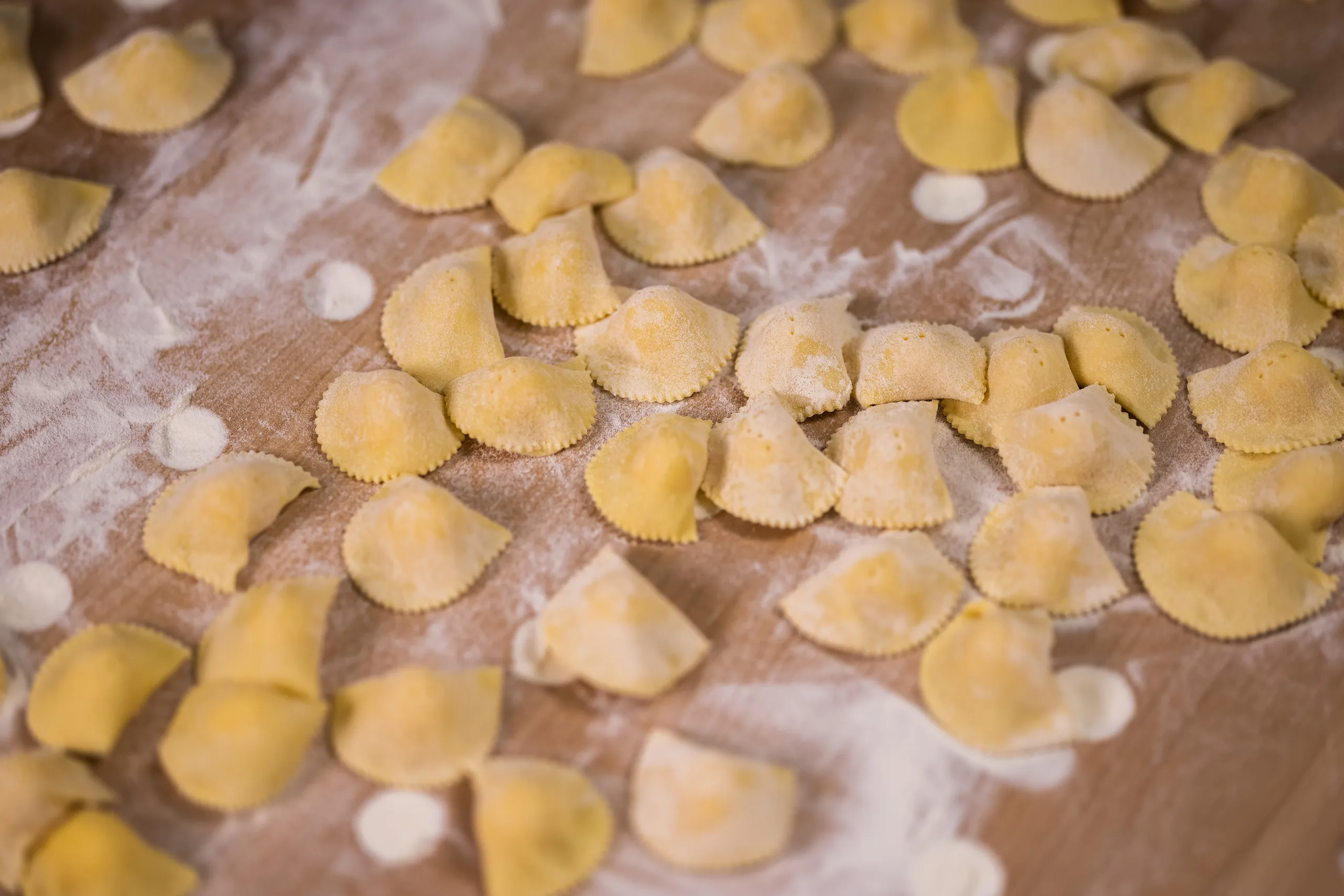 Sveže izdelani ravioli, razporejeni na pomokani leseni deski.